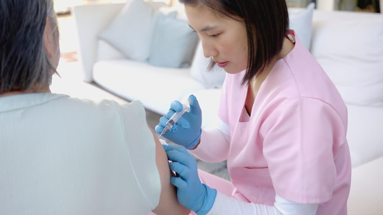 Nurse in pink scrubs administering vaccine to senior patient at home