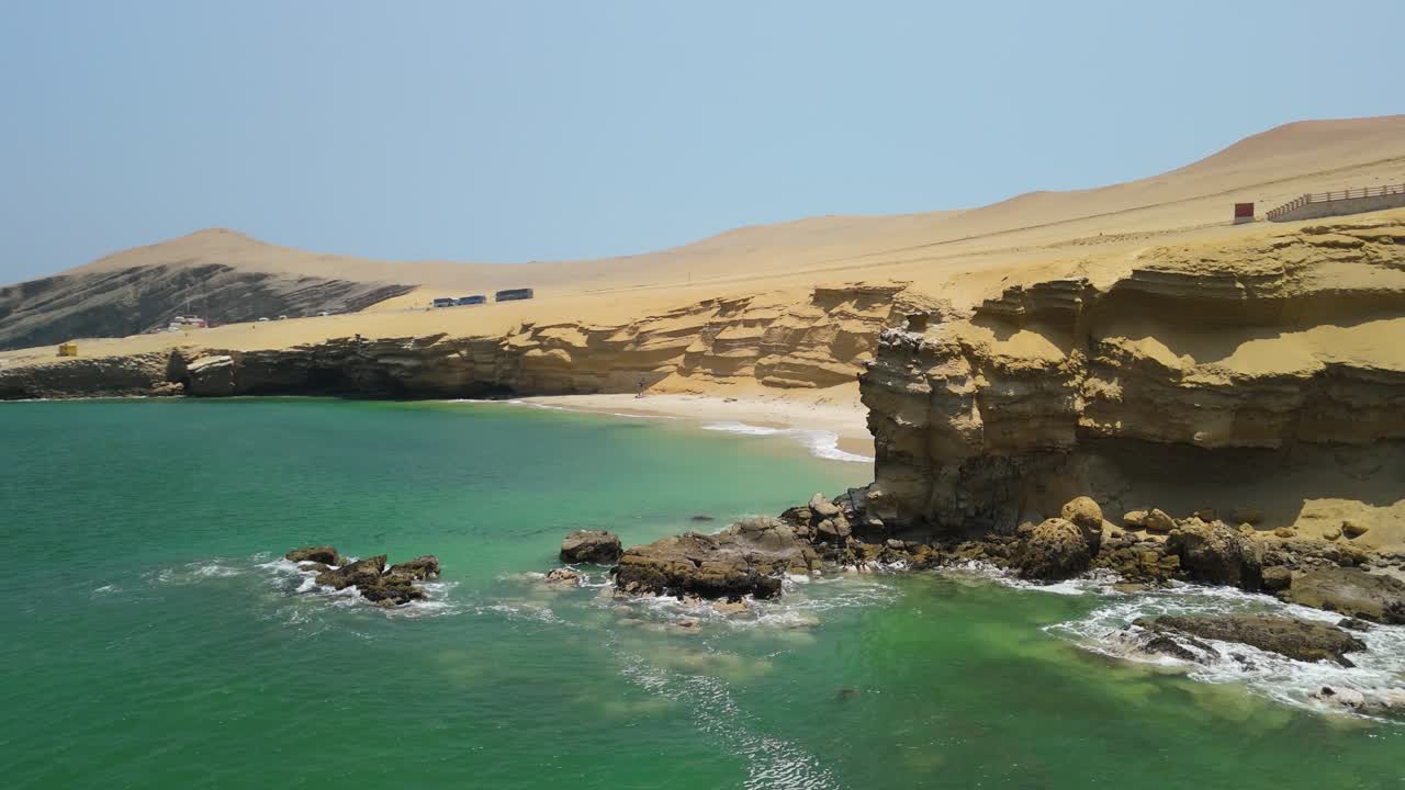 Ripresa aerea con effetto parallasse su Playa La Mina a Paracas con spiaggia sabbiosa, scogliere frastagliate e oceano turchese in Perù
