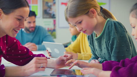 elementary school students and female teacher using digital tablets in classroom lesson