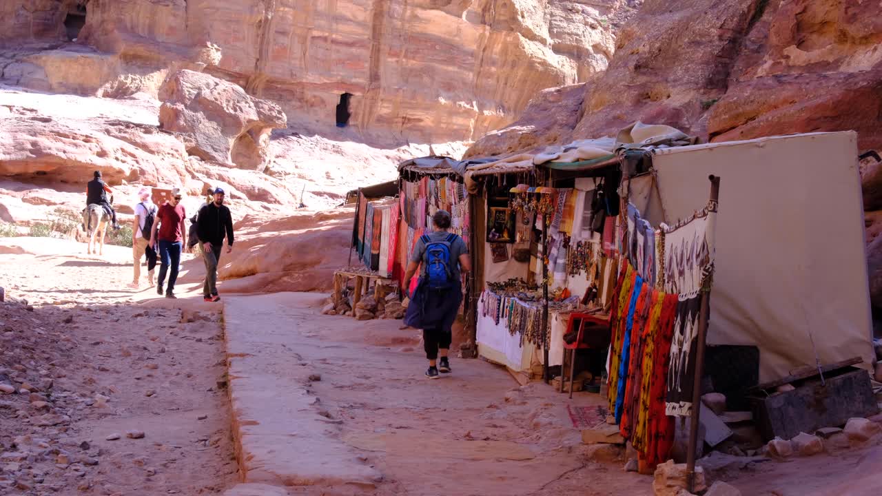 Tourist walking along market stall lined streets through mountainous landscape of ancient city of Petra in Jordan