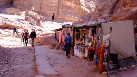 tourist walking along market stall lined streets through mountainous landscape of ancient city of petra in jordan