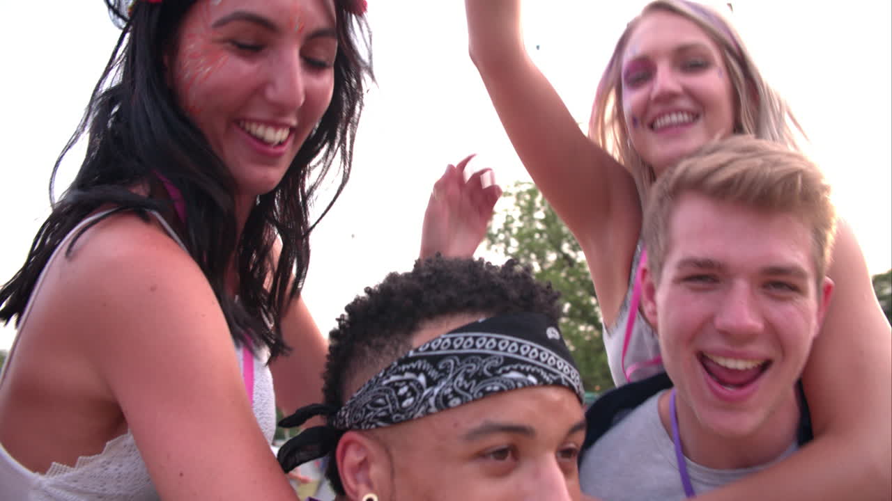 Young friends piggy backing at a music festival, close-up