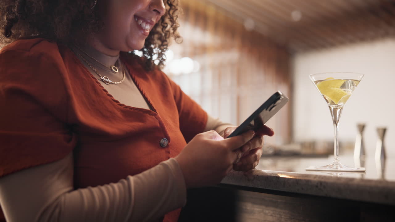 Woman using phone at a bar with a cocktail