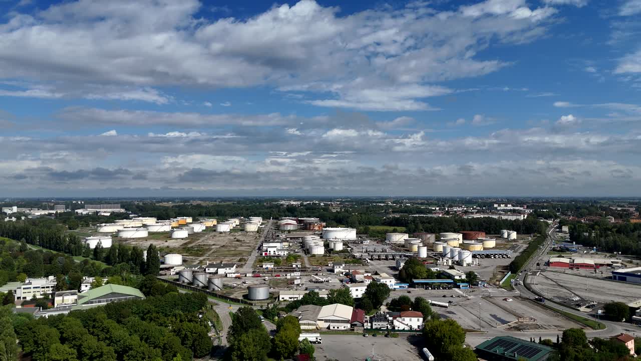 Drone shot over Cremona refinery plant in Lombardy, Italy, featuring extensive storage tanks, industrial buildings, and surrounding greenery under a partly cloudy sky