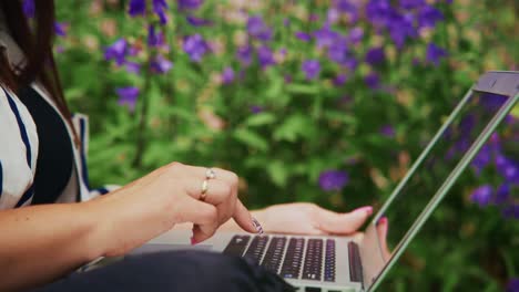 woman typing on laptop outdoors surrounded by vibrant flowers in a serene garden setting