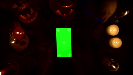 person clicks on a greenscreen smartphone in vertical orientation among halloween decoration