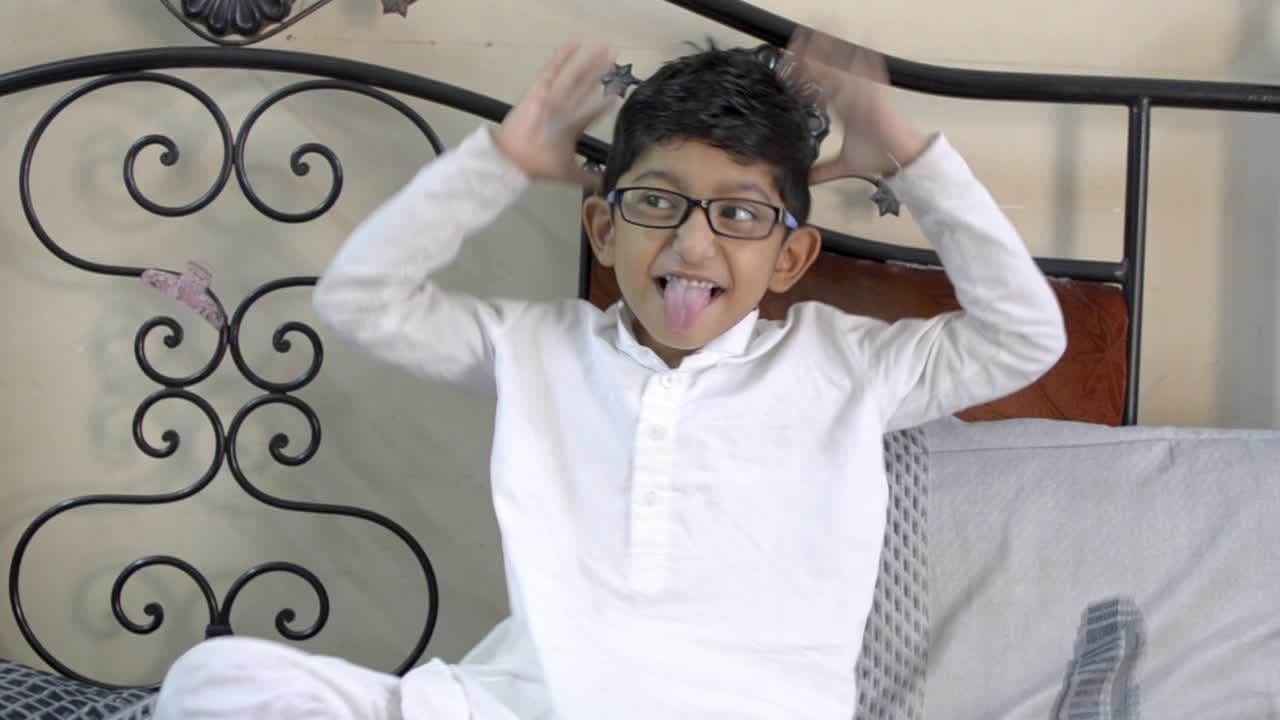 Funny Mocking little boy child tongue out making faces and hand gesture wearing glasses spectacles in living room front view