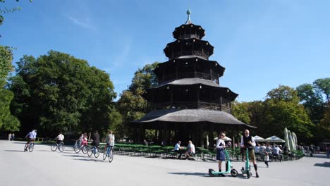 a wide-angle view of munich’s chinese garden park, capturing people strolling through the scenery with a restaurant nestled in the background.