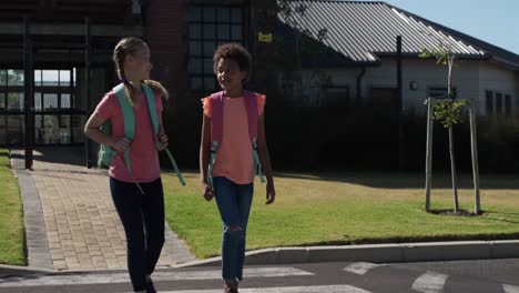 two girls with school bags talking while crossing the road