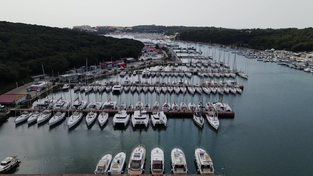 Drone lifts above blue harbor revealing Marina Veruda full of yachts, Croatia