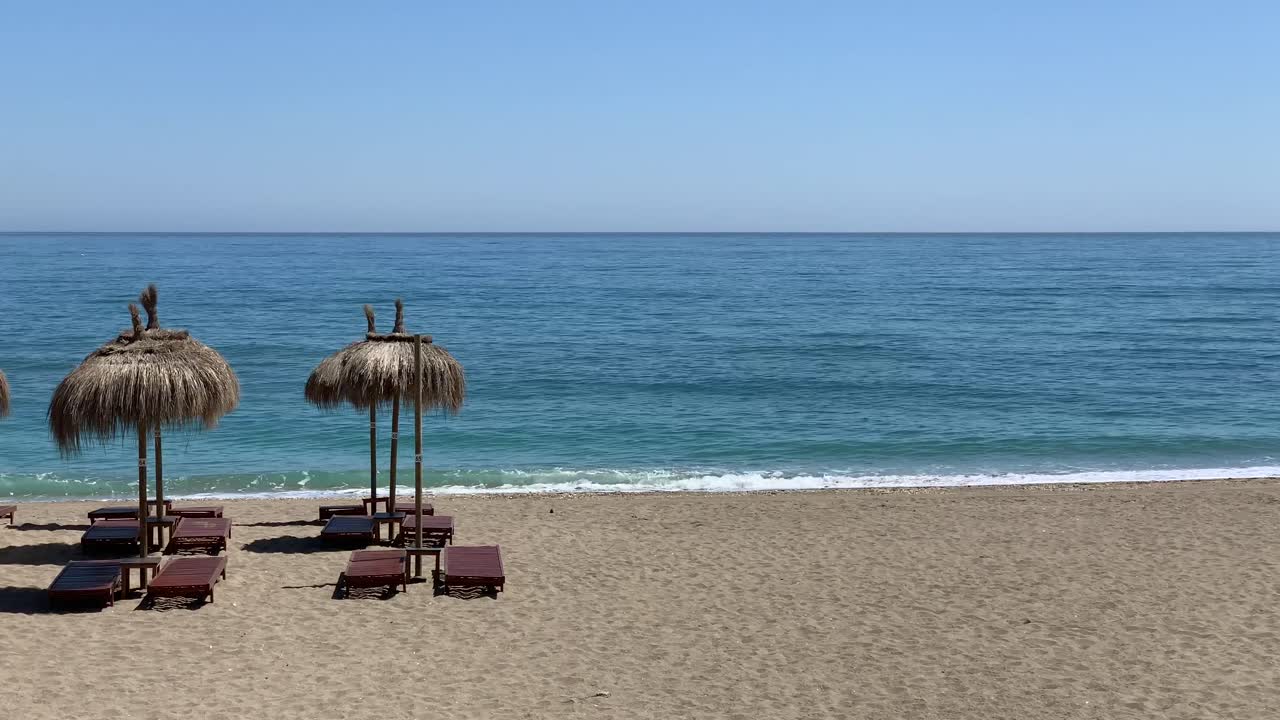 toma estática de la playa con sombrillas estilo tiki tropical en una soleada costa de verano en marbella, malaga, españa, costa del sol