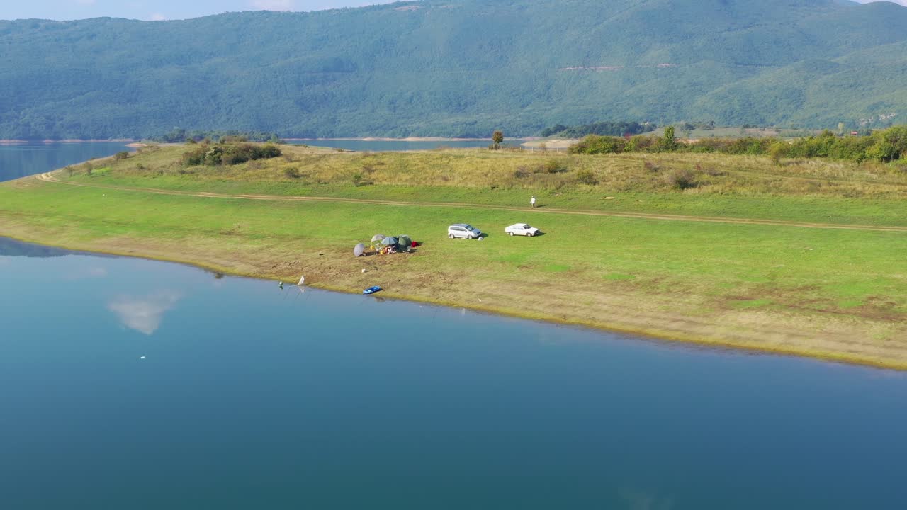 Cars parked on Rama Lake in Bosnia and Herzegovina shore near a small campsite, Aerial dolly in shot