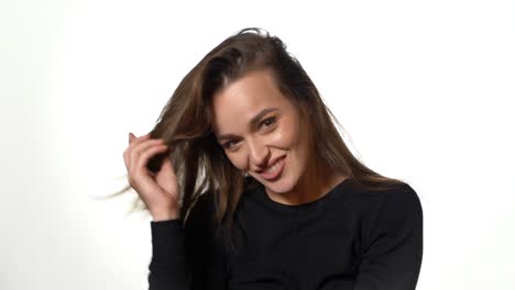 a gorgeous girl in a black jumper is throwing back her hair and smiling on a white background in the studio. close-up