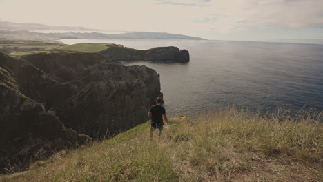 Amplia-Vista-Del-Hombre-Caminando-Al-Borde-Del-Acantilado-En-El-Paisaje-Costero-De-Las-Azores