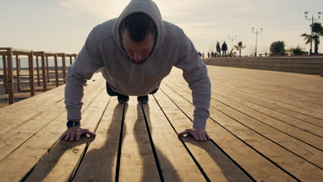 man doing push-ups on a boardwalk by the beach at sunrise/sunset.