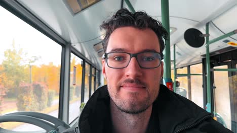 charming european man with a beard and glasses enjoys his journey as a bus passenger in germany, capturing his vibrant experience with a spontaneous selfie toward the camera