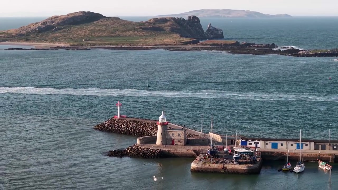Historisk Howth Harbour fyr og marina omgitt av båter i kveldssol. Episk luftfoto