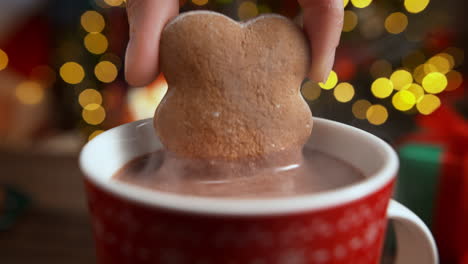 soaking a gingerbread biscuit in a red cup of hot steaming chocolate on christmas eve by the fireplace