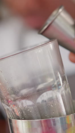 el camarero vierte jugo en una taza de vidrio en un bar de primer plano. el camarero negro agrega ingrediente para un delicioso cóctel en el club. el barman prepara una bebida para los invitados