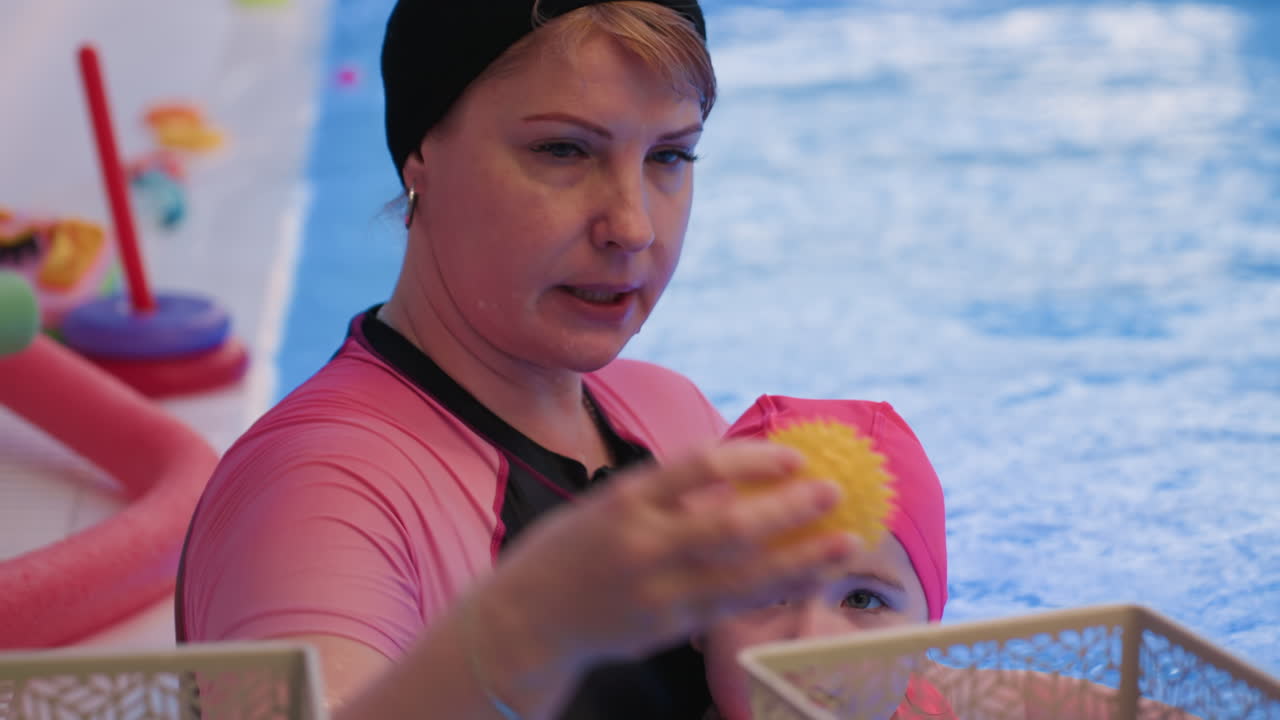 Vorderansicht einer weiblichen Schwimmtrainerin mit konzentriertem Gesichtsausdruck während des Pooltrainings, aufmerksamer Blick, Selbstvertrauen, die Schwimmerin anleitend, Engagement für Sicherheit, Coaching, klarer Wasserhintergrund, weiches Licht auf den Gesichtszügen