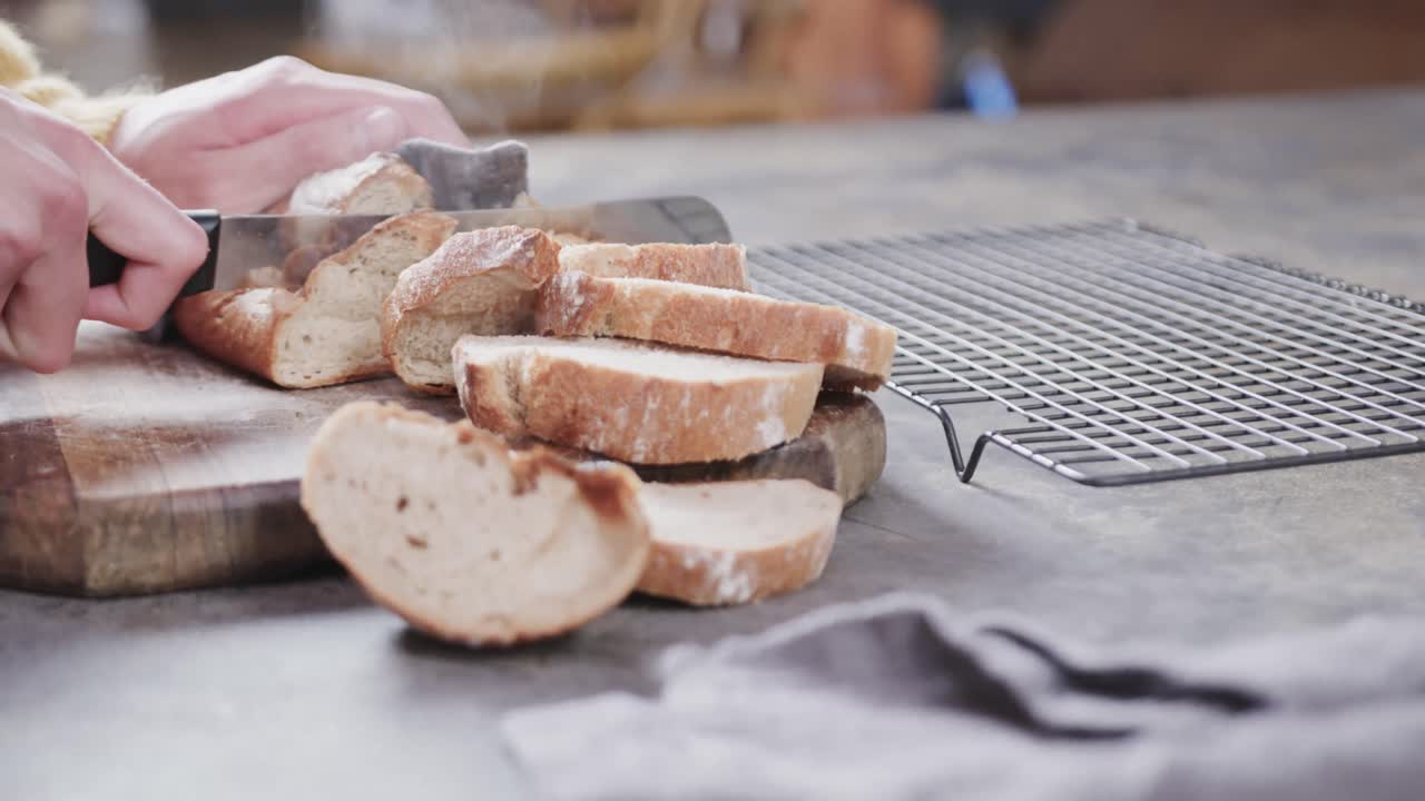 Hands of caucasian man cutting bread in kitchen, slow motion