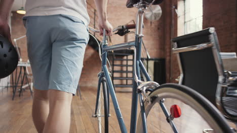 Young-businessman-arriving-at-work-pushing-bicycle-carrying-helmet