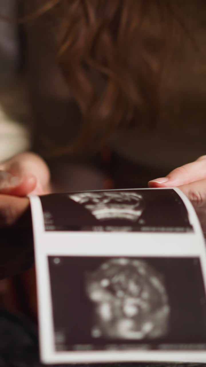 White woman and African-American boyfriend future parents examine ultrasound pictures of human embryo in living room extreme closeup slow motion