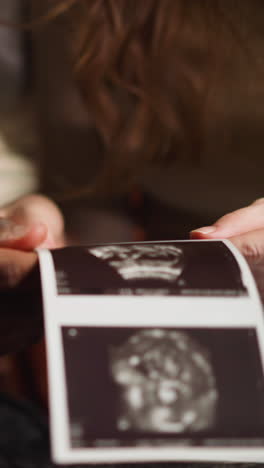 white woman and african-american boyfriend future parents examine ultrasound pictures of human embryo in living room extreme closeup slow motion