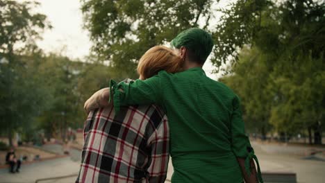 A-blonde-girl-with-a-short-haircut-in-a-plaid-shirt-leaned-on-the-shoulder-of-her-girlfriend-with-a-green-short-haircut-in-a-Green-shirt-sitting-on-the-fence-in-a-skate-park-in-the-summer.-Happy-LGBT-couple-during-their-date