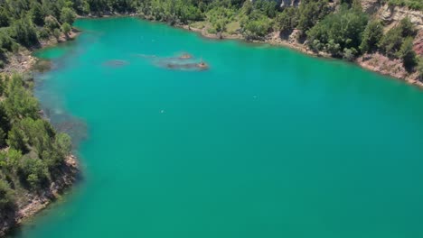 drone aéreo volando sobre un vibrante lago turquesa rodeado de árboles con pájaros volando sobre él