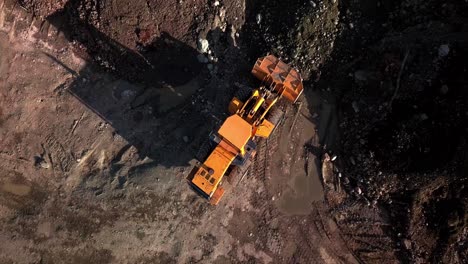 Large-powerful-yellow-mining-wheel-operating-loader-lifts-brown-dirt-on-ground-in-Yukon,-Canada,-directly-above-aerial-circle