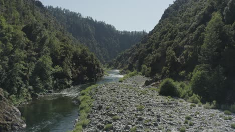 slow drone flight over a rocky river surrounded by lush forest