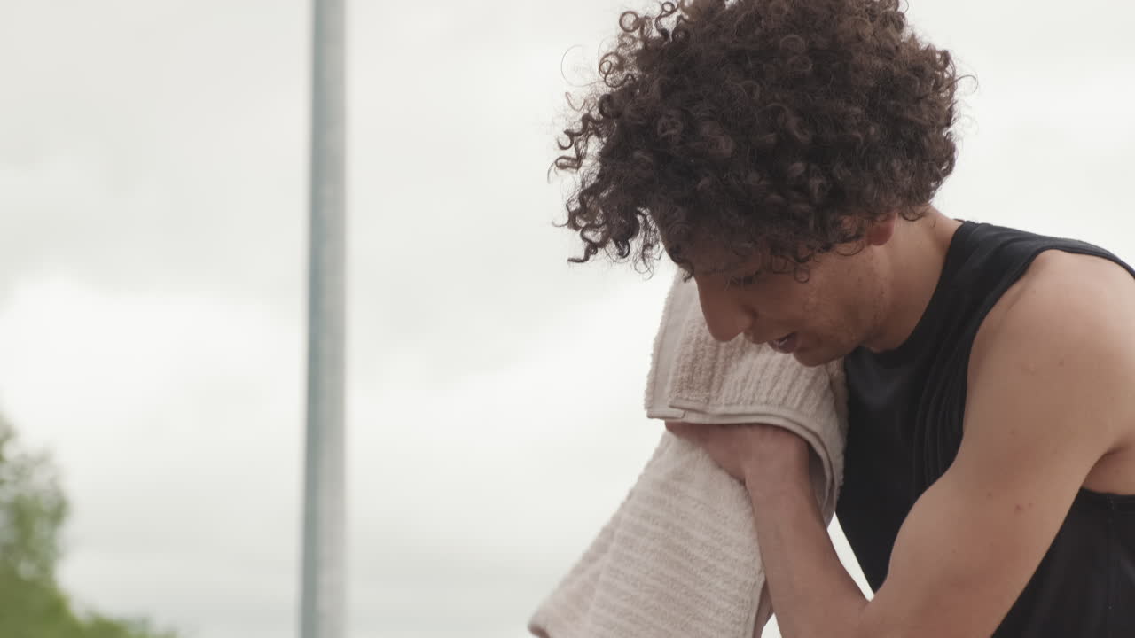 Man with curly hair using a towel to wipe sweat