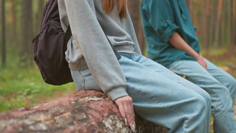 close-up of two tired hikers resting on fallen tree in serene forest setting, focused on their relaxed posture with one leaning on tree for support, amidst lush greenery