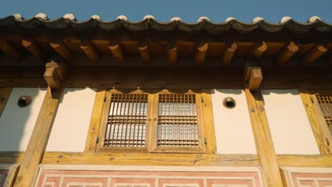 sunlight reflects on wooden lattice windows beneath a tiled roof of a hanok in bukchon hanok village, jongno-gu, seoul. low angle shot