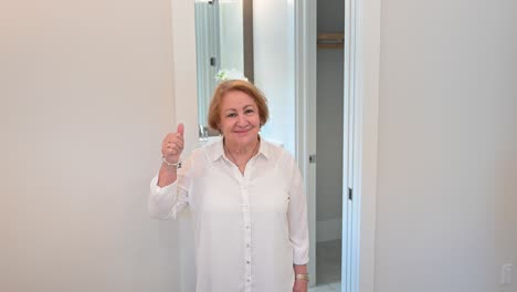 una mujer mayor en un dormitorio blanco da un pulgar hacia arriba de aprobación con sus amantes de lujo.