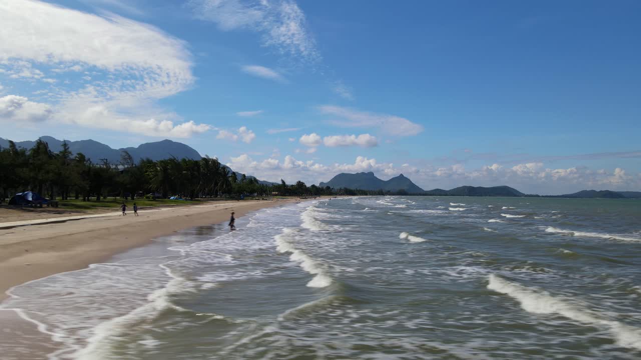 Metraje aéreo deslizante de las olas que se precipitan hacia la orilla revelando la playa y algunas personas silueteadas