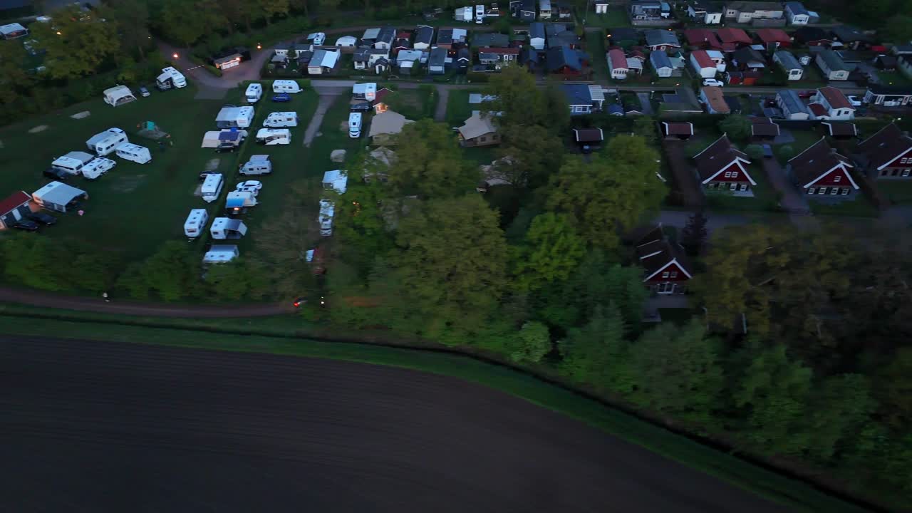 Campground with tent, camper vans and mobile trailer homes in american suburbia. Car on street along farm fields at night. Aerial top down shot.