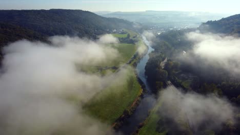 morning light hits the valley where a river is flowing through, while clouds are moving above it in the countryside of luxembourg