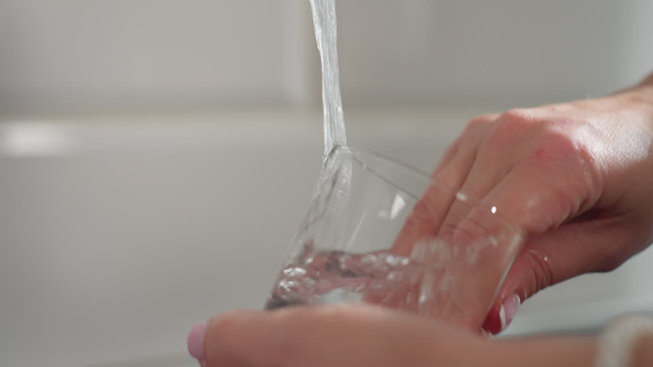 Close up of glass cup being thoroughly rinsed with neat water while person hand is inside cleaning rim showing focus on hygiene, cleanliness