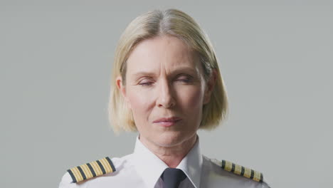 studio portrait of serious mature female airline pilot or ship captain against plain background