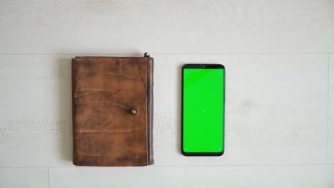phone with green screen on the table with notebook and purse view from top, smartphone chromakey screen copy space