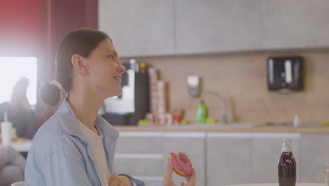 side view of pregnant woman sitting at table eating a donut and talking with coworker in canteen