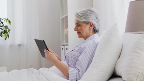 Senior-Woman-with-Tablet-Pc-in-Bed-at-Home-Bedroom.technology,-old-age-and-people-concept--senior-woman-with-tablet-pc-computer-in-bed-at-home-bedroom