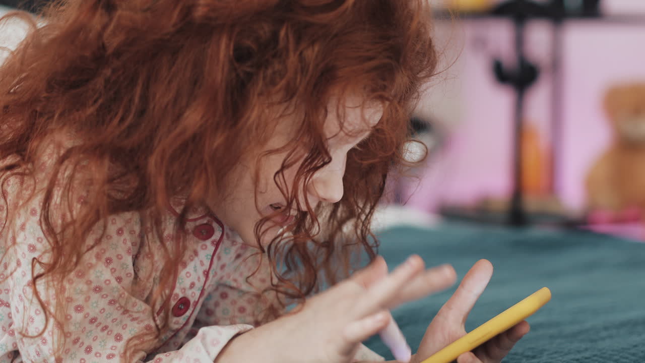 Little girl playing on her phone in bed