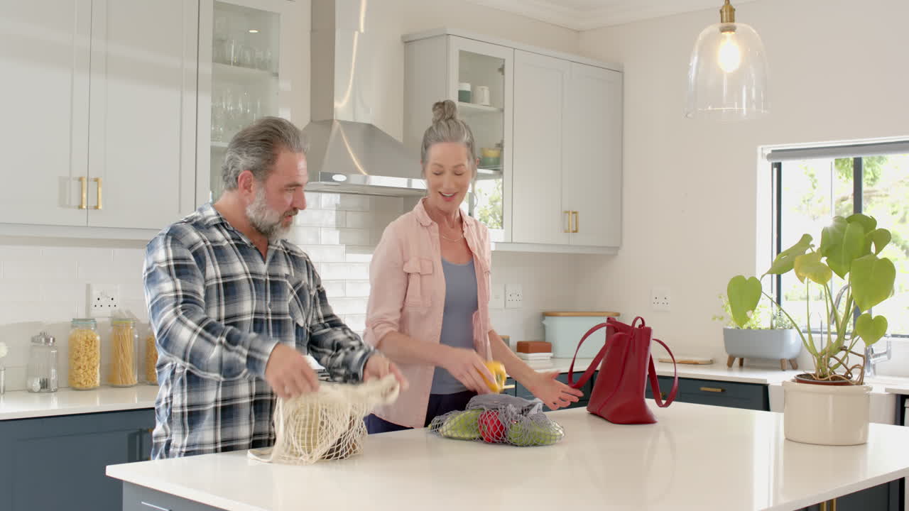 Unpacking groceries in modern kitchen, mature couple smiling and talking together