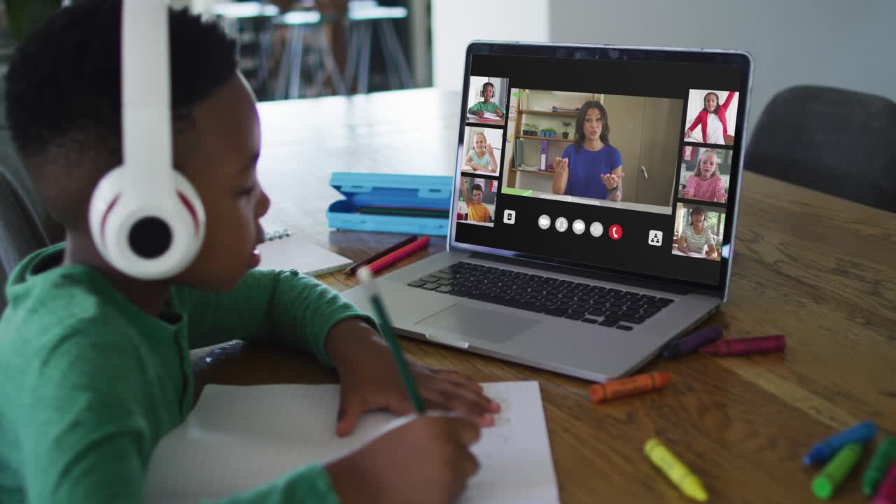 Schoolboy using laptop for online lesson at home, with diverse teacher and class on screen