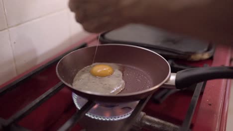 old person breaking eggs on frying pan