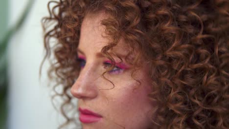 professional hair stylist finishing modeling hairdo to young smilling girl customer with red coloured hair and perfect pink makeup. hairdresser woman making final touch to ginger long curly hair. close up