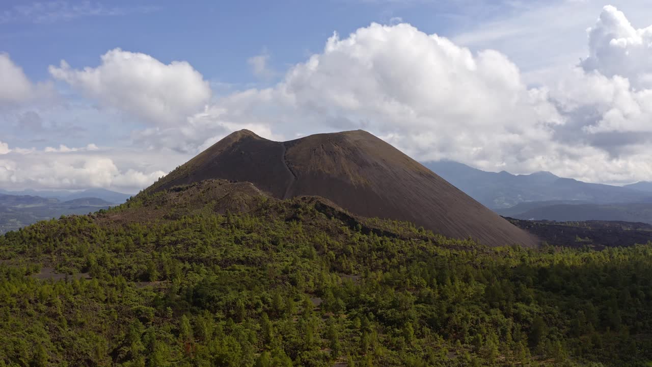 Parícutin Volcano rises through clouds with a lush green forest in the foreground